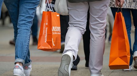Menschen mit vollen Einkaufstaschen gehen an den Geschäften vorbei. / Foto: Monika Skolimowska/dpa