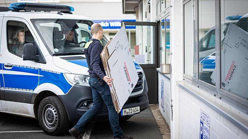 Ein Polizeibeamter geht während einer Durchsuchung an einem Polizeiwagen vorbei. / Foto: Moritz Frankenberg/dpa