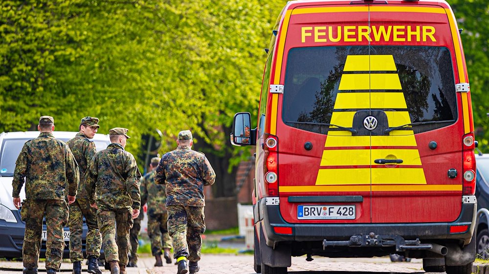 Soldaten der Bundeswehr gehen eine Straße in einem Wohngebiet entlang, vorbei an einem Einsatzfahrzeug der Feuerwehr. / Foto: Moritz Frankenberg/dpa