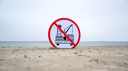 Ein Plakat gegen die geplante Erdgasförderung steht im Sand. / Foto: Sina Schuldt/dpa/Archivbild