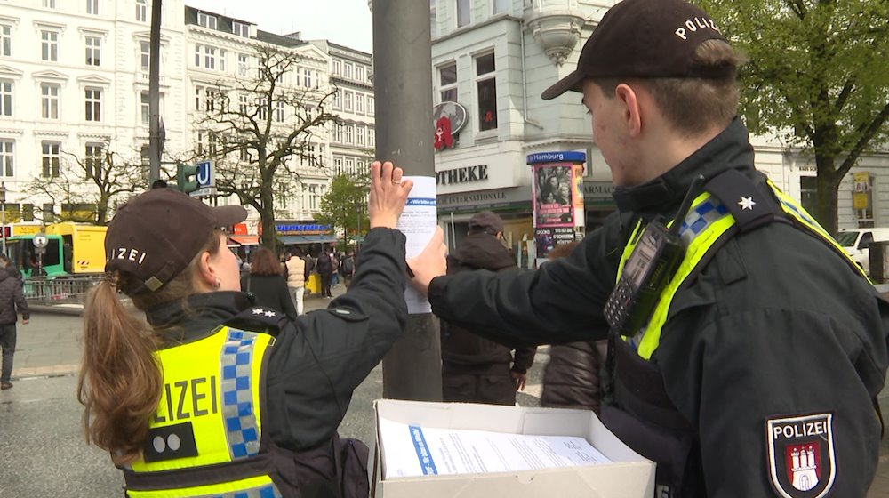 Mitarbeiter der Polizei befestigen einen Zettel für eine Zeugensuche an einem Laternenpfosten. / Foto: Steven Hutchings/-/dpa
