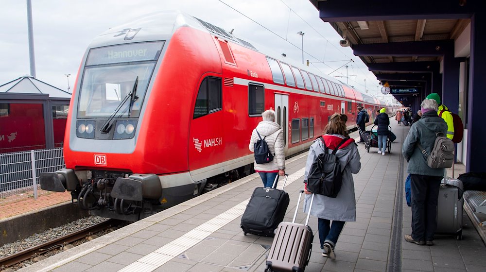 Touristen laufen mit Rollkoffern am Bahnhof Norddeich-Mole entlang. / Foto: Philip Dulian/dpa/Archivbild