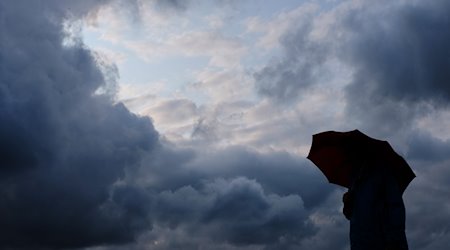 Ein Mann geht bei stark bewölktem Himmel mit einem Regenschirm spazieren. / Foto: Martin Gerten/dpa