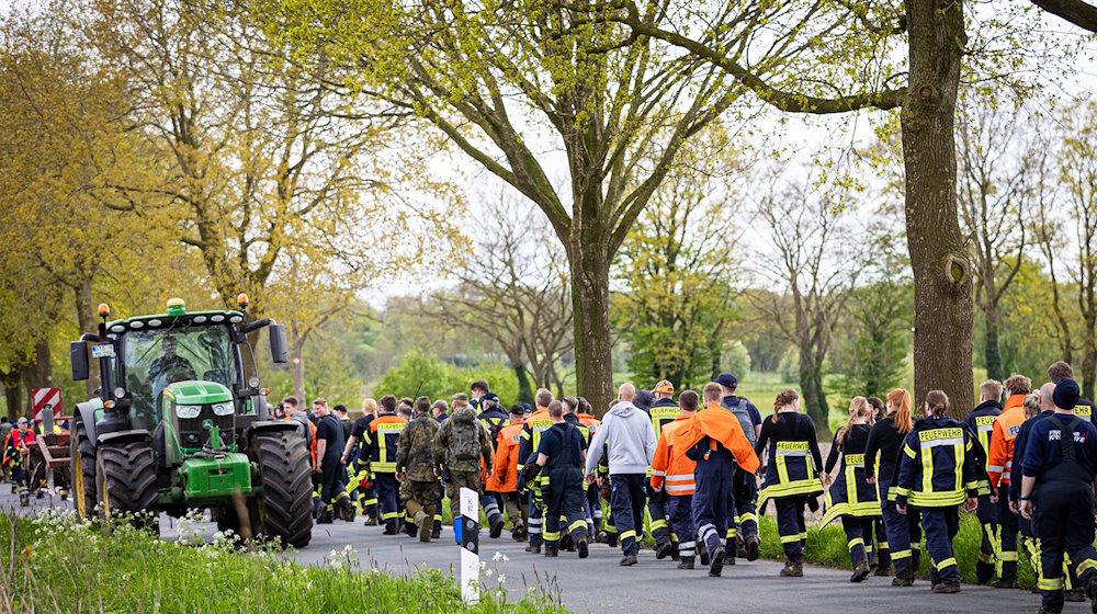 Einsatzkräfte der Feuerwehr gehen eine Straße im Landkreis Stade entlang. / Foto: Moritz Frankenberg/dpa