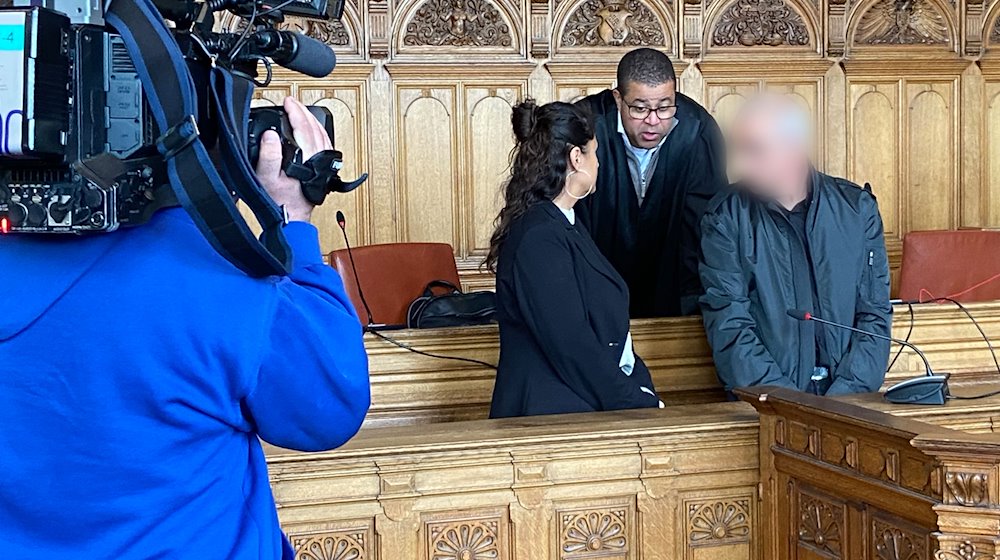 Der Angeklagte (r) steht vor Beginn des Prozesses mit seinem Anwalt Temba Hoch (hinten) und einer Dolmetscherin im Gerichtssaal im Landgericht Bremen. / Foto: Janet Binder/dpa