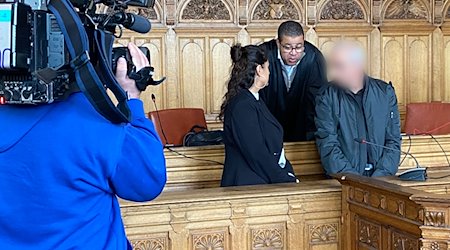 Der Angeklagte (r) steht vor Beginn des Prozesses mit seinem Anwalt Temba Hoch (hinten) und einer Dolmetscherin im Gerichtssaal im Landgericht Bremen. / Foto: Janet Binder/dpa