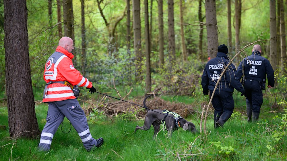 Einsatzkräfte des Deutschen Roten Kreuzes sind mit einem Suchhund in einem Waldstück im Einsatz. / Foto: Daniel Reinhardt/dpa