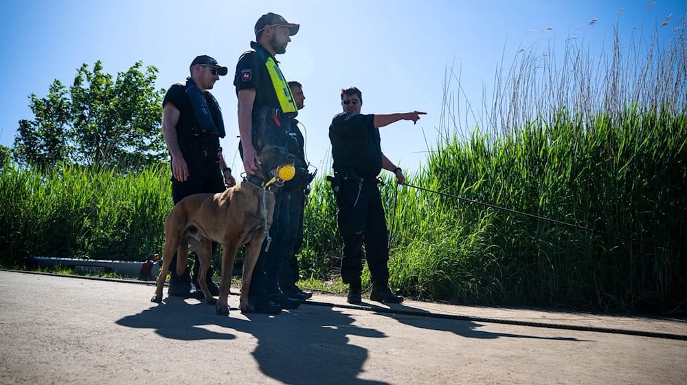 Einsatzkräfte der Polizei stehen bei der Suche nach dem vermissten Arian mit einem Spürhund an der Oste. / Foto: Sina Schuldt/dpa