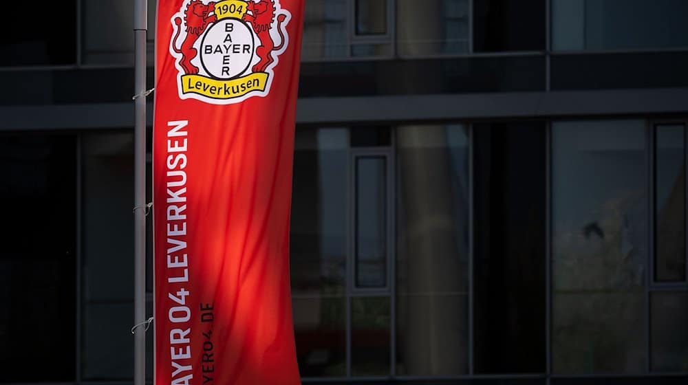 Eine Fahne weht vor der BayArena, dem Stadion des Fußball-Bundesligisten Bayer 04 Leverkusen, und wird dabei von der Sonne angeschienen. / Foto: Marius Becker/dpa