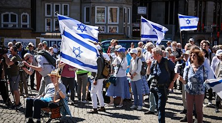 Teilnehmer einer Kundgebung der deutsch-israelischen Gesellschaft Bremen/Unterweser zum Unabhängigkeitstag des Staates Israel stehen mit israelischen Flaggen auf dem Marktplatz in Bremen. / Foto: Focke Strangmann/dpa