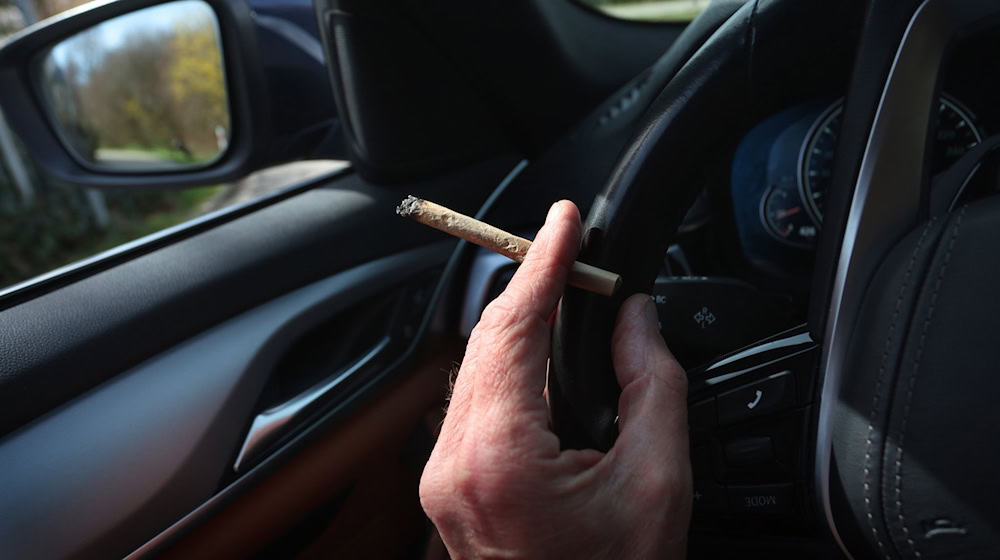 Ein Mann sitzt mit einem Joint zwischen den Fingern am Steuer eines Autos. / Foto: Karl-Josef Hildenbrand/dpa