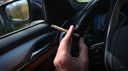 Ein Mann sitzt mit einem Joint zwischen den Fingern am Steuer eines Autos. / Foto: Karl-Josef Hildenbrand/dpa