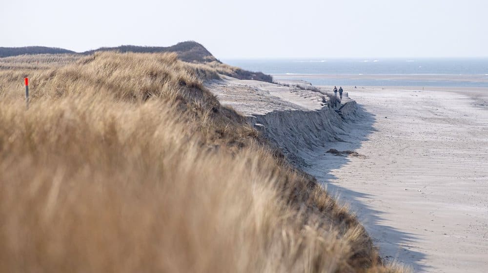 Spaziergänger laufen an der Abbruchkannte am Strand entlang. / Foto: Sina Schuldt/dpa/Archiv