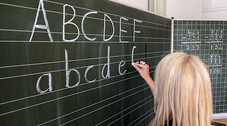 Eine Grundschullehrerin schreibt die ersten Buchstaben des Alphabets auf eine Schultafel in einem Klassenzimmer. / Foto: Axel Heimken/dpa/Archivbild