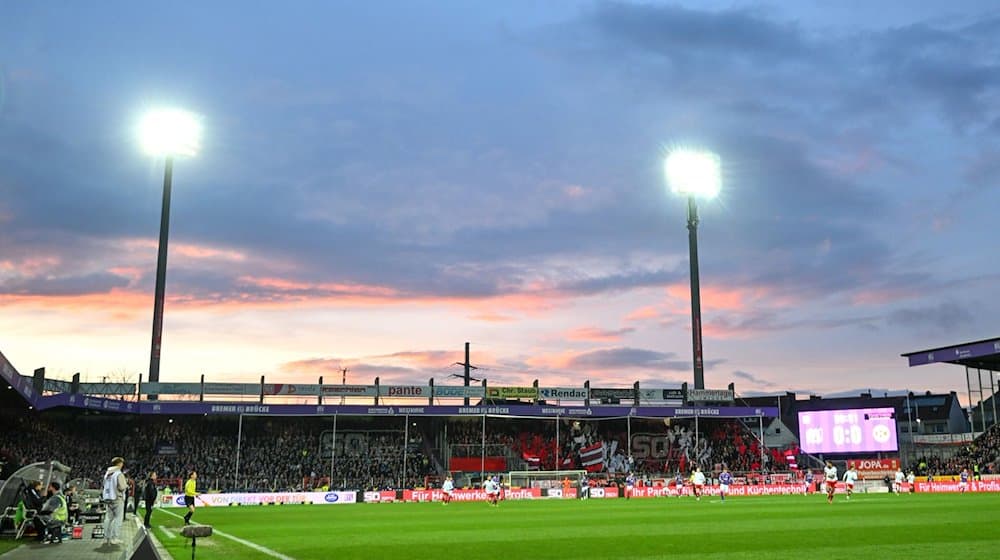 Flutlicht scheint auf das Spielfeld, während im Hintergrund die Sonne untergeht. / Foto: Titgemeyer/osnapix/dpa