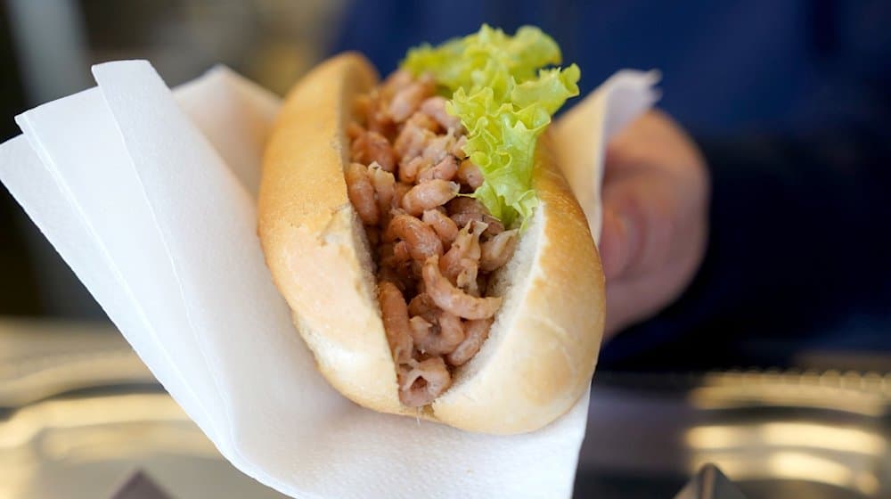 Ein Mitarbeiter reicht einem Kunden ein Brötchen mit Nordseekrabben über den Tresen eines Fischbrötchen-Imbisses. / Foto: Marcus Brandt/dpa/Illustration