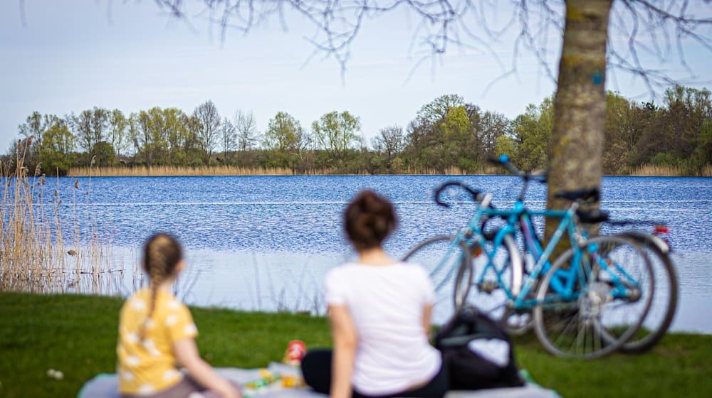 Eine Frau und ein Kind sitzen bei sonnigem Wetter am Ufer vom Hufeisensee. / Foto: Moritz Frankenberg/dpa