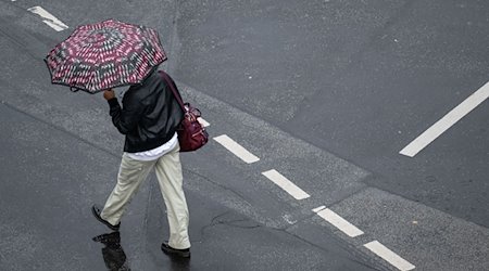 Mit einem Schirm schützt sich eine Passantin vor dem Regen. / Foto: Boris Roessler/dpa/Symbolbild