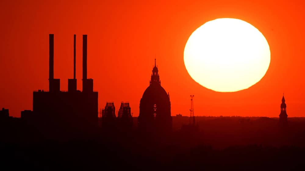 Die Sonne geht hinter dem Gaskraftwerk Linden und dem Neuen Rathaus unter. / Foto: Julian Stratenschulte/dpa