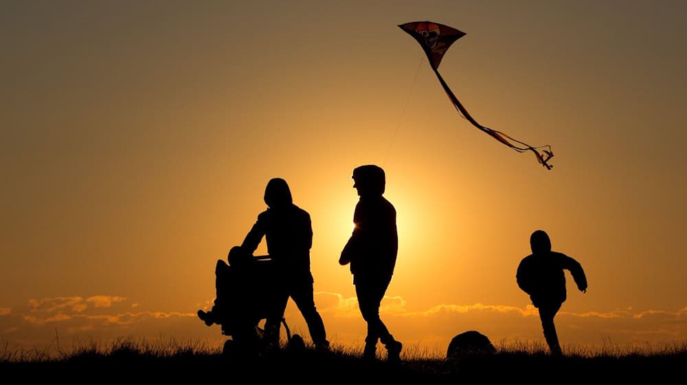 ILLUSTRATION - Eine Familie geht bei Sonnenuntergang über einen Weg. / Foto: Christian Charisius/dpa