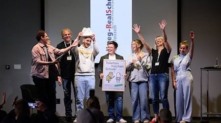 Abgesandte der Hellweg Realschule in Unna-Massen (Nordrhein-Westfalen) stehen zusammen mit Moderator "Checker" Julian Janssen (l) bei der Verleihung der Hauptpreise des bundesweiten Wettbewerbs "Toiletten machen Schule" beim 1. Deutschen Schultoilettengipfel der German Toilet Organization (GTO) auf der Bühne. / Foto: Bernd von Jutrczenka/dpa