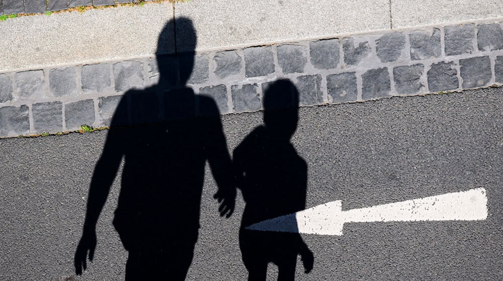 Der Schatten von einem Mann und einem Kind sind auf einer Straße mit einem Pfeil zu sehen. / Foto: Julian Stratenschulte/dpa/Archivbild