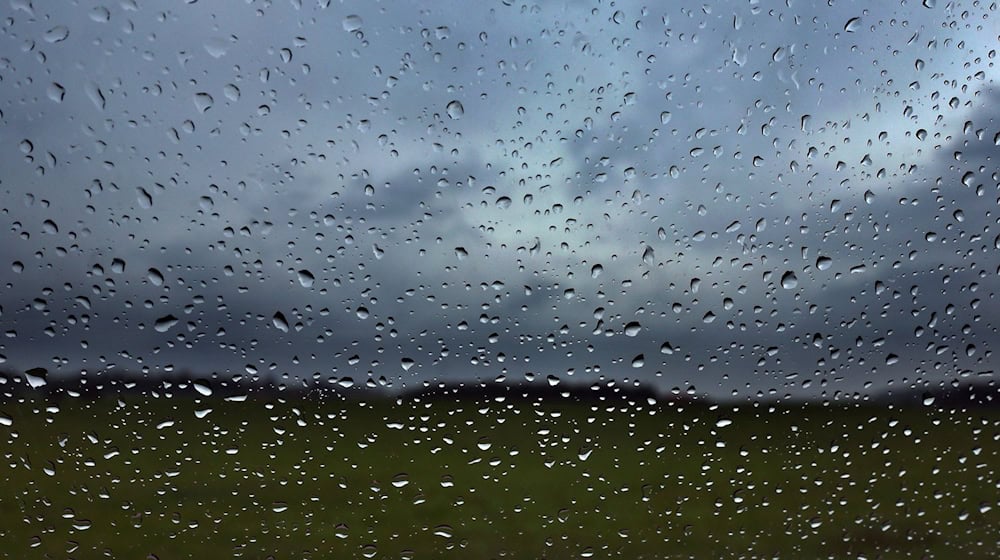 Eine Autoscheibe ist vor dunklen Wolken mit Regentropfen bedeckt. / Foto: Karl-Josef Hildenbrand/dpa