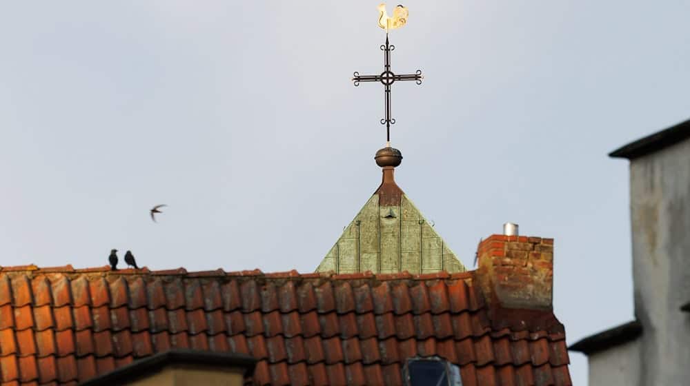Ein Kreuz vom katholischen Dom St. Petrus ist im Licht der untergehenden Sonne zu sehen. / Foto: Friso Gentsch/dpa