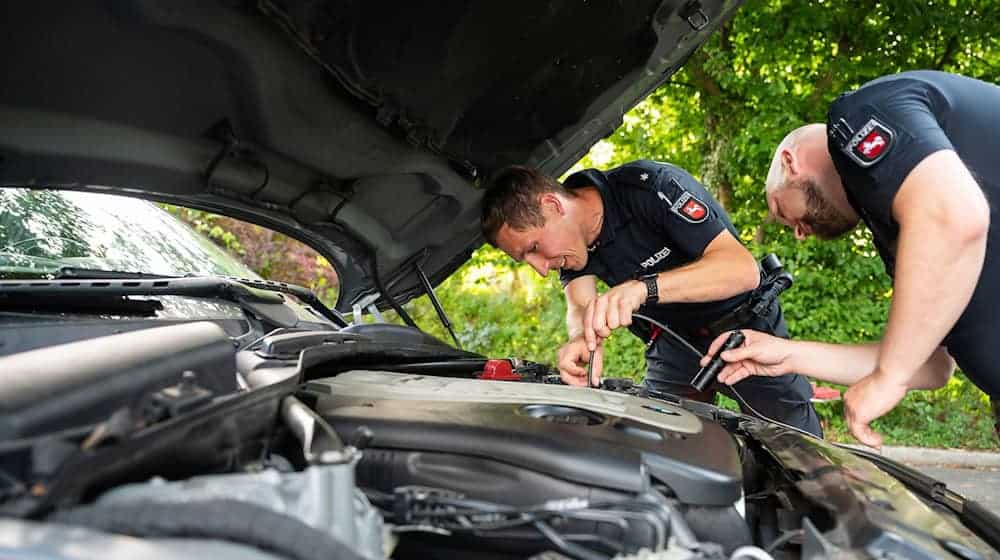 Zwei Polizisten der Arbeitsgruppe "Auto-Poser" schauen in den Motorraum eines Fahrzeuges. / Foto: Philipp Schulze/dpa