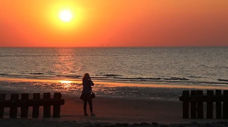 Eine Frau fotografiert am Strand der Insel Wangerooge einen Sonnenuntergang. / Foto: Peter Kuchenbuch-Hanken/dpa/Symbolbild