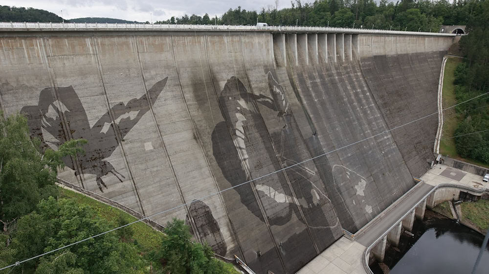 Auf der Staumauer der größten Trinkwassertalsperre Deutschlands wird mit Hochdruckreinigern ein Kunstwerk gemalt. / Foto: Matthias Bein/dpa