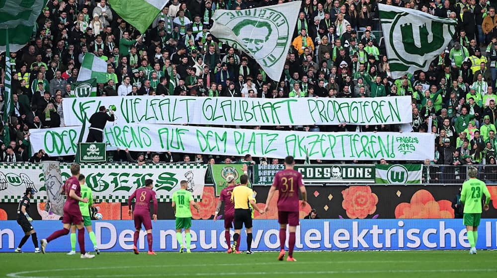 Wolfsburgs Fans mit einem Banner mit der Aufschrift «VfL Vielfalt glaubhaft propagieren - oder Behrens auf dem Platz akzeptieren». / Foto: Swen Pförtner/dpa