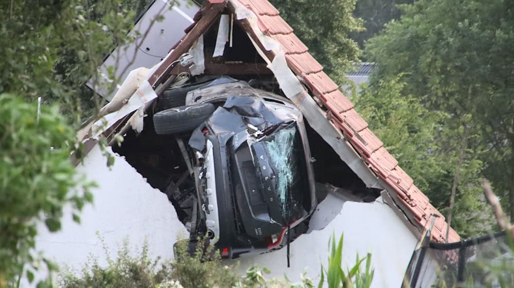 Ein Auto liegt nach einem kurzen Flug seitlich in der Mauer einer Scheune. / Foto: -/Moonshine Media/dpa