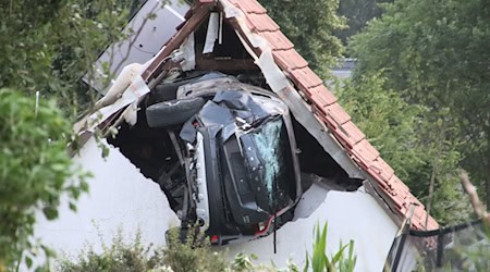 Ein Auto liegt nach einem kurzen Flug seitlich in der Mauer einer Scheune. / Foto: -/Moonshine Media/dpa