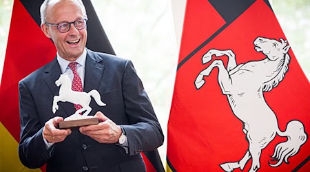 Doppelt im Bild: Pferde auf der Krawatte und eines in der Hand. Bundeskanzler Merz mit Gastgeschenk in der Staatskanzlei. / Foto: Moritz Frankenberg/dpa