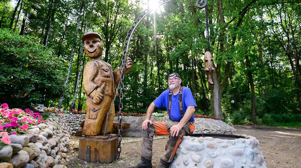 Motorsägenkünstler Andree Löbnitz neben einer Holzskulptur, die er aus einem Holzstamm schnitzte. / Foto: Philipp Schulze/dpa
