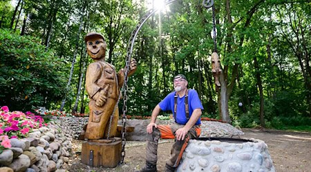 Motorsägenkünstler Andree Löbnitz neben einer Holzskulptur, die er aus einem Holzstamm schnitzte. / Foto: Philipp Schulze/dpa