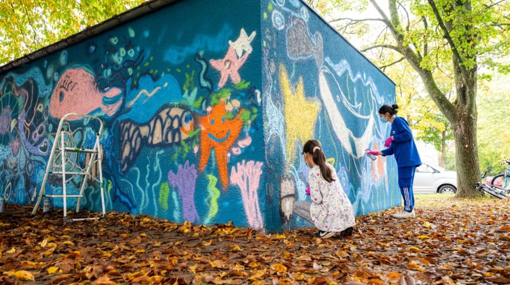 Kinder aus der Nachbarschaft gestalten gemeinsam eine bunte Unterwasserwelt mitten im Quartier Dodesheide. Bildnachweis: Vonovia / Bierwald