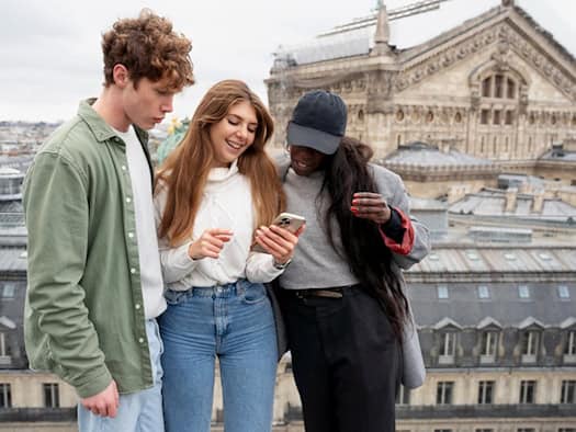 Drei junge Menschen betrachten gemeinsam ein Smartphone in einer Großstadt – lokale Suche und digitale Entdeckungen im urbanen Raum.
