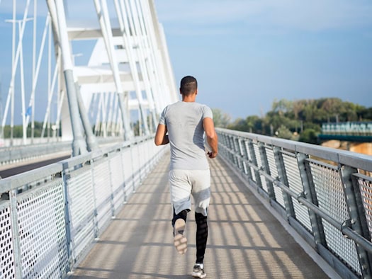 Ein Sportler in grauer Sportkleidung läuft allein über eine moderne Brücke mit Metallgeländer, symbolisiert den Übergang in eine neue Phase – vom aktiven Sport in die nächste Karriereetappe.