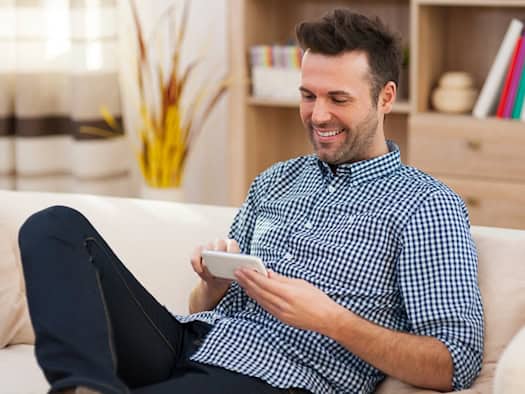 Lächelnder Mann nutzt ein Smartphone auf dem Sofa – entspanntes Gaming-Erlebnis mit Mikro-Belohnungen.
