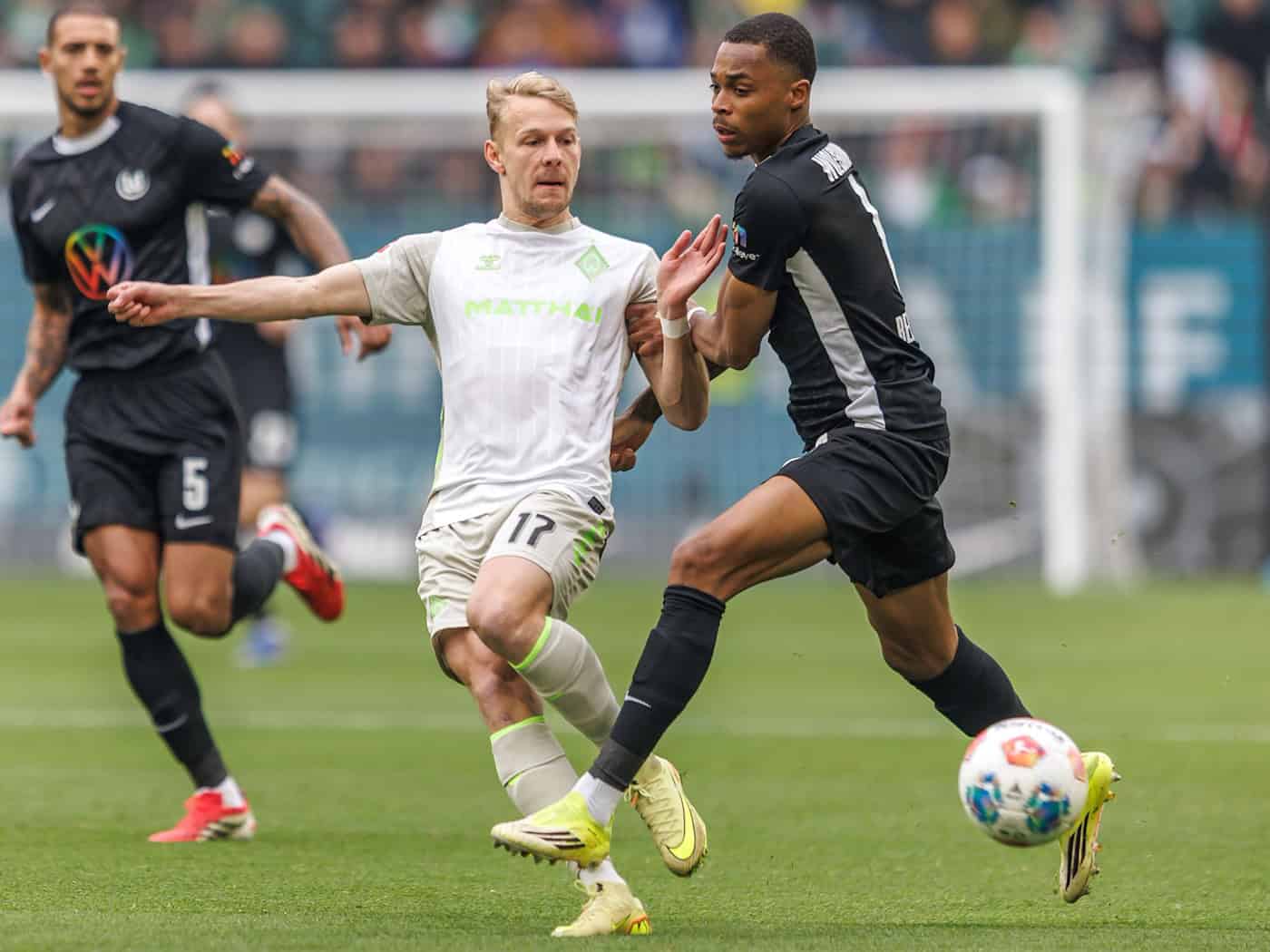 Werders Marco Grüll (l) wird von Wolfsburgs Jeanuel Belocian bedrängt. / Foto: Andreas Gora/dpa