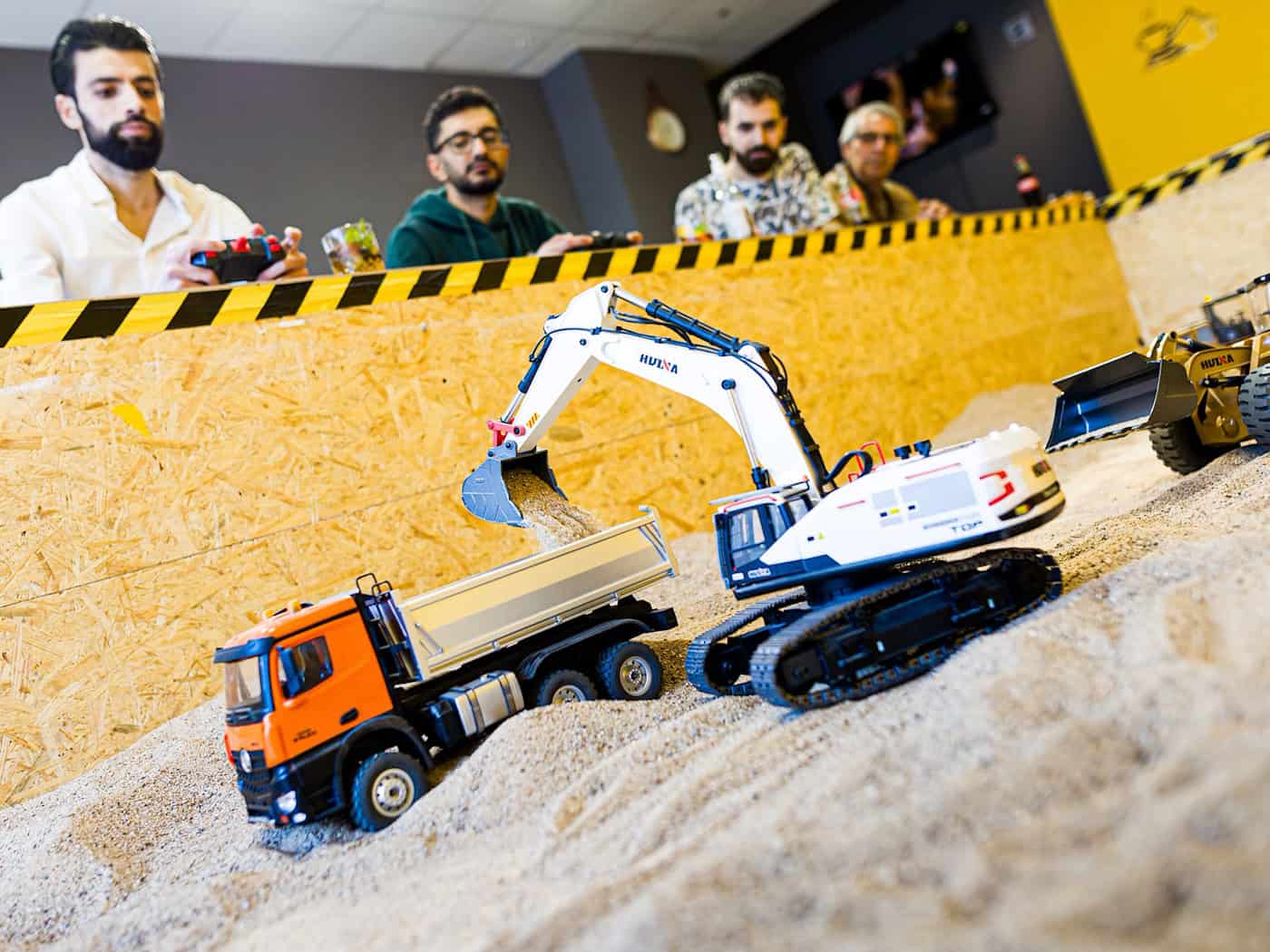 Gründer Siymo Othman (links) steuert mit Freunden kleine Bagger, Radlader und Lastwagen in seinem neu eröffneten Bagger-Café. Es soll das erste dieser Art in Deutschland sein. / Foto: Moritz Frankenberg/dpa