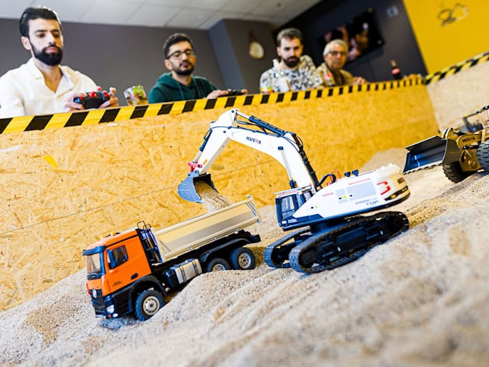 Gründer Siymo Othman (links) steuert mit Freunden kleine Bagger, Radlader und Lastwagen in seinem neu eröffneten Bagger-Café. Es soll das erste dieser Art in Deutschland sein. / Foto: Moritz Frankenberg/dpa