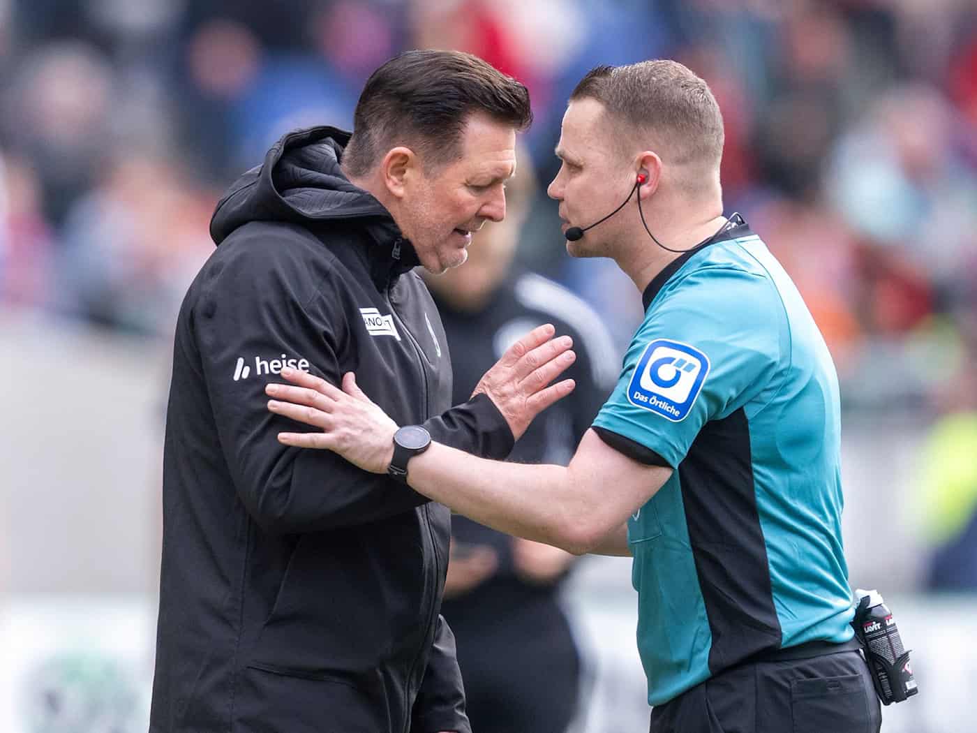 96-Trainer Christian Titz (l) spricht mit Schiedsrichter Robert Kampka. / Foto: David Inderlied/dpa