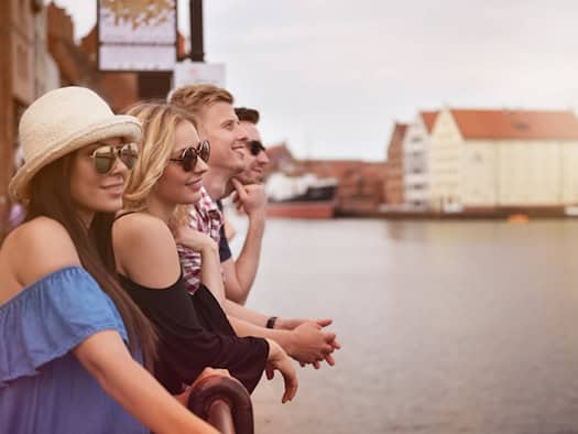 Vier entspannte Menschen genießen gemeinsam einen sonnigen Kurzurlaub am Wasser mit Blick auf historische Gebäude.