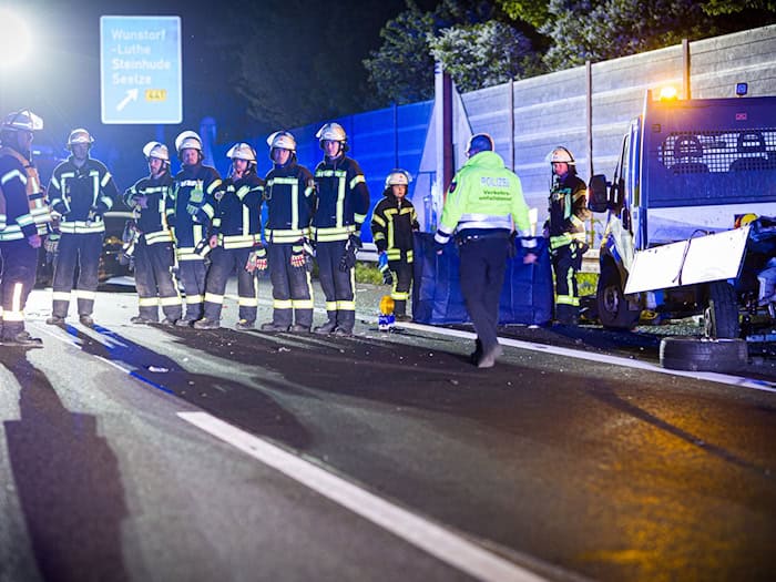 Einsatzkräfte der Feuerwehr stehen in der Nacht neben dem Baustellenfahrzeug in einer Reihe, um für vorbeifahrende Autofahrer einen Sichtschutz zu bilden.  / Foto: Moritz Frankenberg/dpa