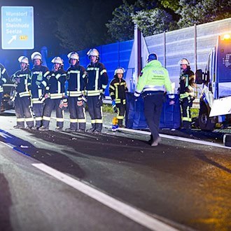 Einsatzkräfte der Feuerwehr stehen in der Nacht neben dem Baustellenfahrzeug in einer Reihe, um für vorbeifahrende Autofahrer einen Sichtschutz zu bilden.  / Foto: Moritz Frankenberg/dpa