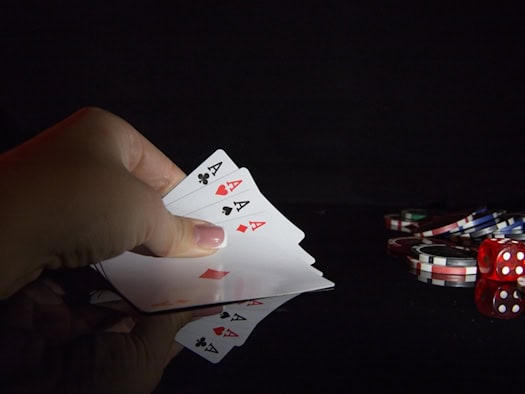 Hand hält vier Asse im Kartenspiel mit Spielchips und Würfeln auf dem Tisch