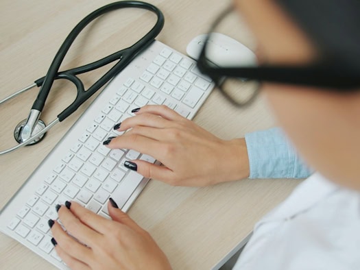 Ärztin tippt auf einer Tastatur mit Stethoskop daneben – Telemedizin in der Praxis